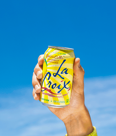 A hand holding a can of LimonCello LaCroix sparking water naturally essenced 12 fl with a clear blue sky background.
